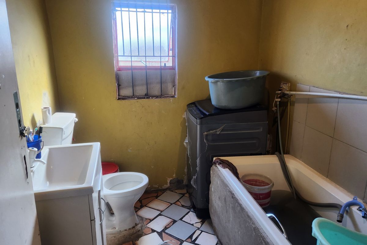 A small bathroom featuring a bathtub, vanity basin, and toilet, requiring significant cosmetic updates and repairs to the wall finishes and flooring.