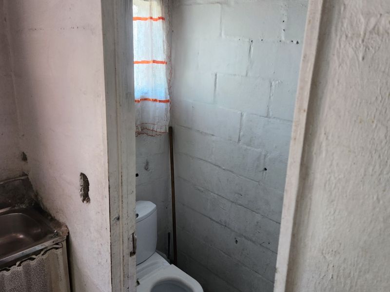 A small, basic bathroom featuring a toilet and sink with unfinished exposed blockwork walls, requiring renovation and cosmetic updates.