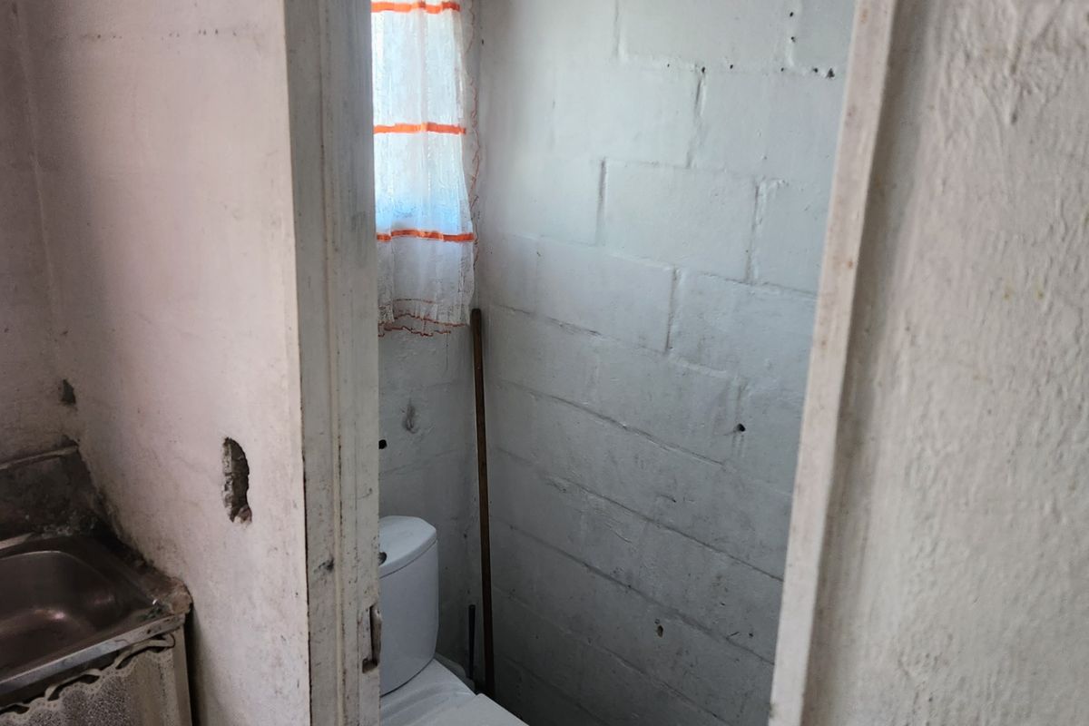 A small, basic bathroom featuring a toilet and sink with unfinished exposed blockwork walls, requiring renovation and cosmetic updates.