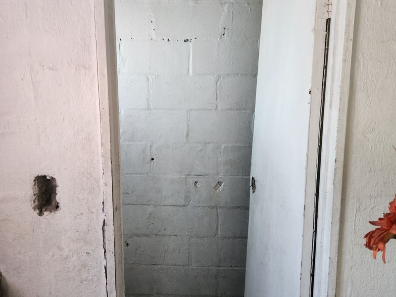 A small, unfinished bathroom space featuring exposed concrete block walls and tiled flooring, requiring significant cosmetic renovation and repair.