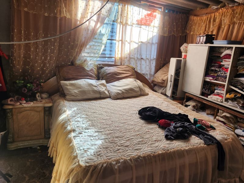 A bedroom featuring exposed ceiling beams and louvered windows, requiring significant renovation to improve the structural finish and overall condition of the space.