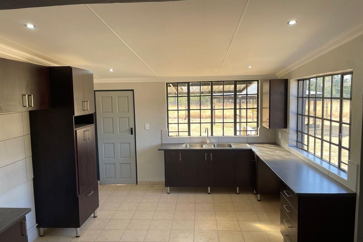 A functional, empty kitchen featuring dark wood cabinetry, laminate countertops, a stainless steel double sink, and tiled flooring with ample natural light.
