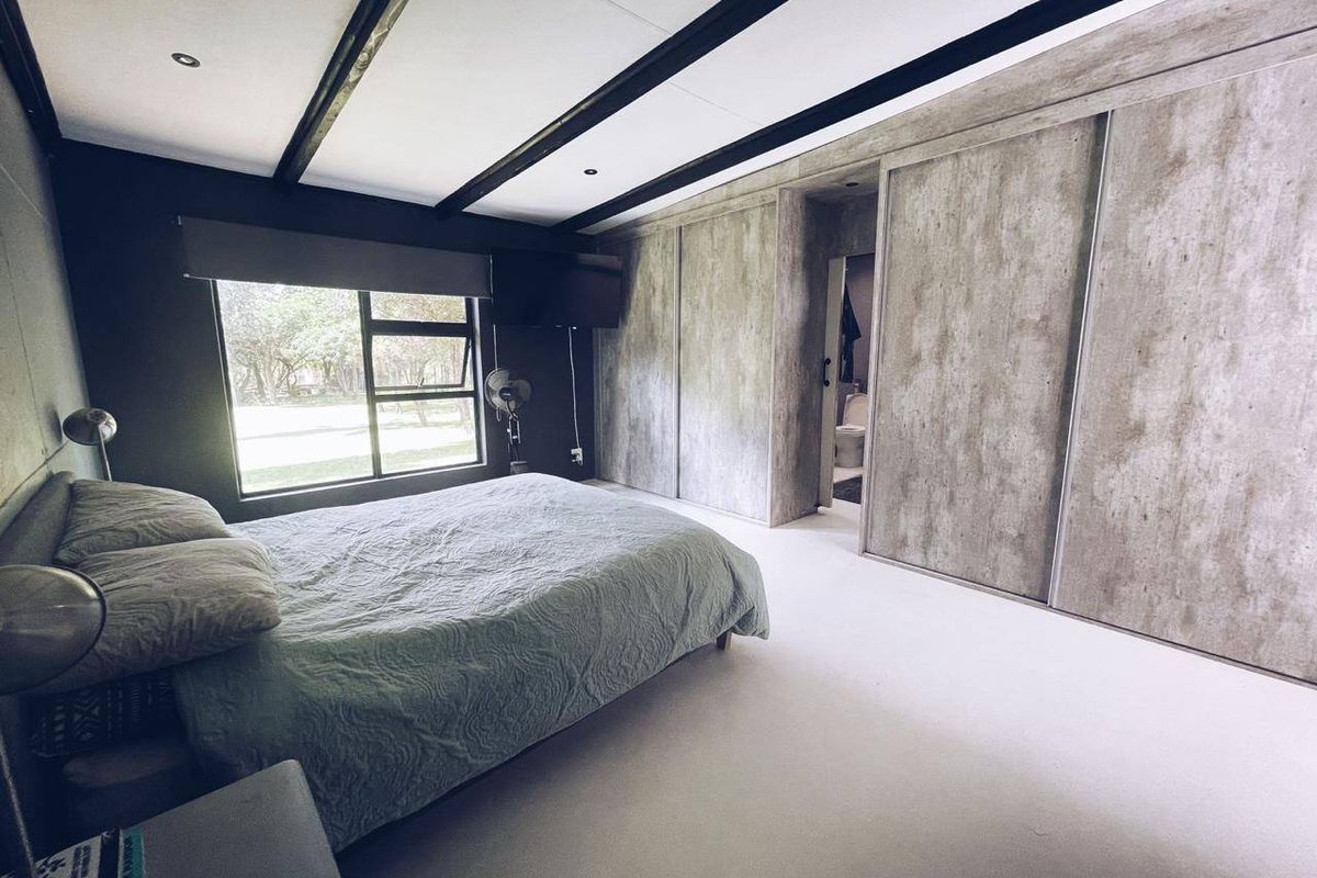 Modern bedroom featuring exposed ceiling beams, recessed lighting, and extensive built-in sliding door wardrobes with a concrete-effect finish.