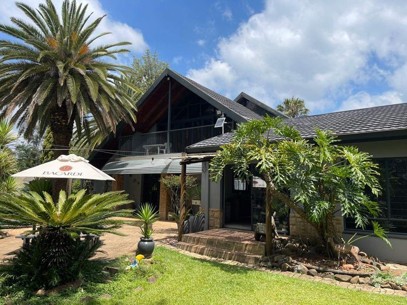 Rear view of a multi-level house featuring a tiled roof, stone cladding, a balcony, and a paved patio area set within a landscaped garden.