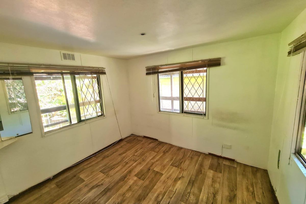 An empty bedroom featuring laminate flooring, security bars on windows, and venetian blinds, requiring minor cosmetic repairs to walls and baseboards.