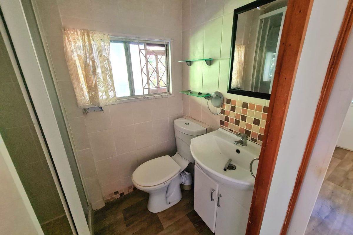 A compact bathroom featuring a vanity cabinet, toilet, and shower enclosure with tiled walls and security bars on the window.