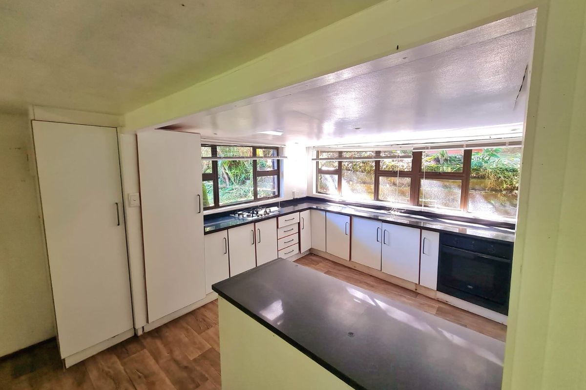 A functional, empty kitchen featuring white cabinetry, dark countertops, a built-in oven, gas hob, and large windows overlooking the garden.