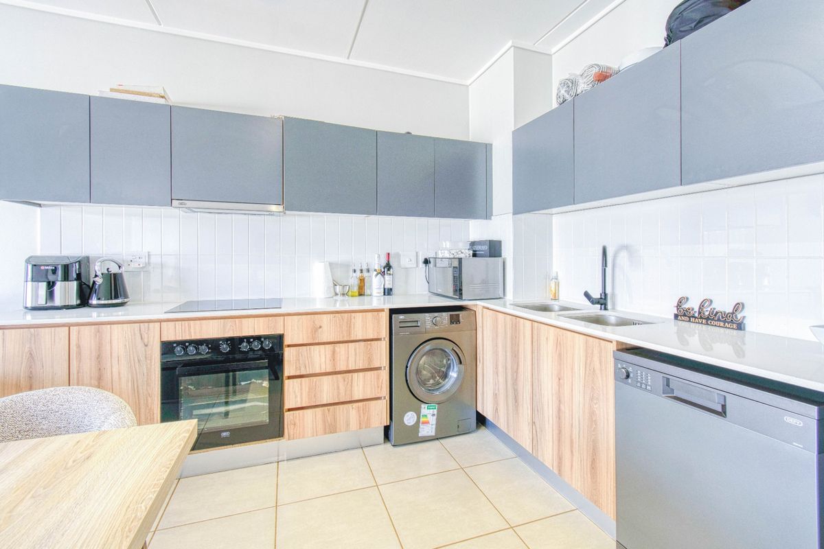 Modern kitchen featuring wood-grain and grey cabinetry, built-in oven, electric hob, double sink, and integrated laundry appliance space.