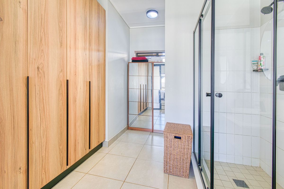 A modern bathroom featuring light wood-finish built-in cabinetry, a glass-enclosed shower, and neutral floor tiles.