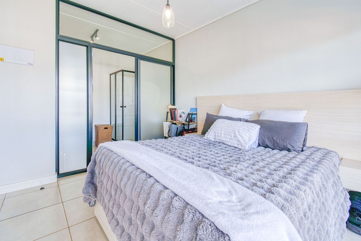A modern bedroom featuring a built-in headboard, tiled flooring, and a sleek glass partition wall leading to an en-suite shower area.