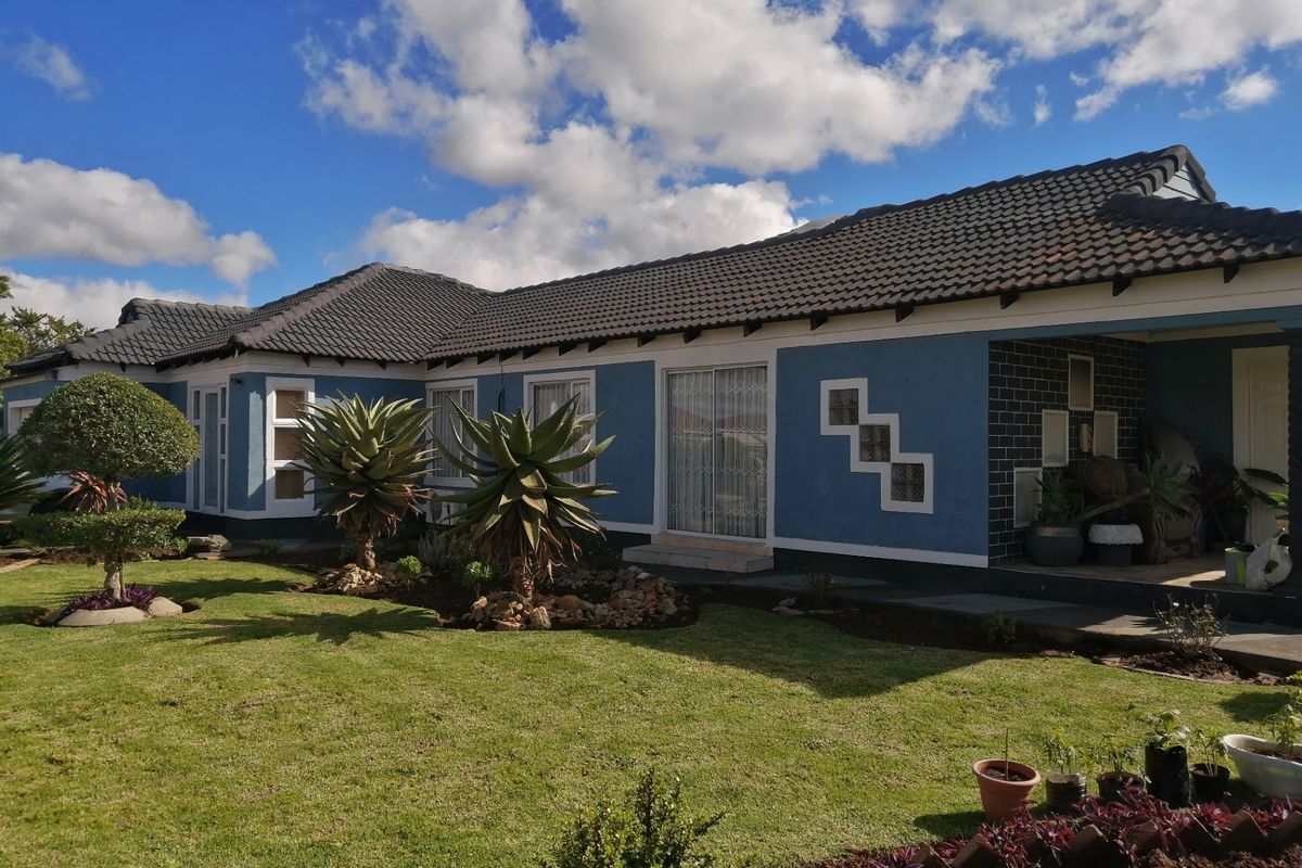 Rear view of the house featuring a well-maintained lawn, covered patio area, and blue exterior walls with decorative glass block accents.