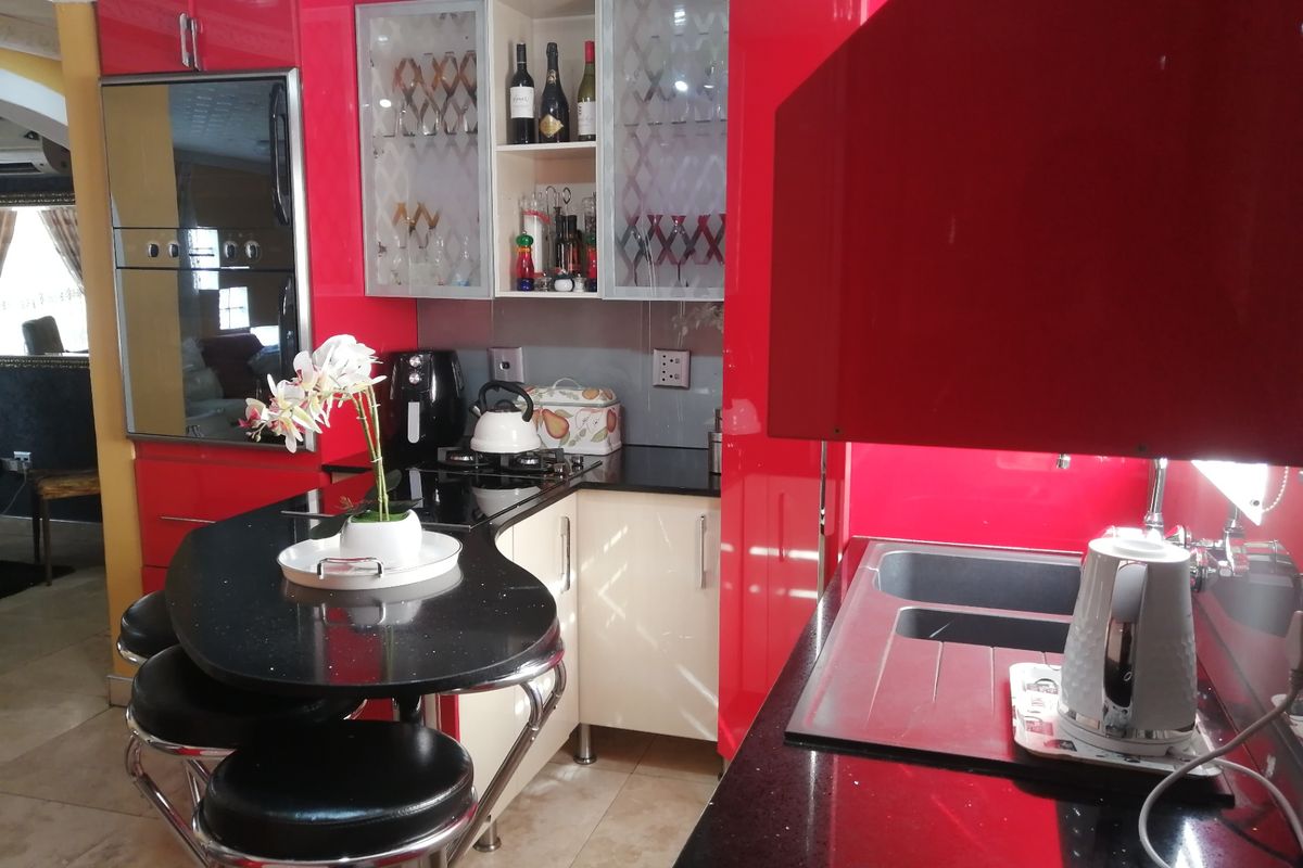 A vibrant kitchen featuring high-gloss red cabinetry, black granite countertops, integrated oven, and a breakfast bar area with tiled flooring.