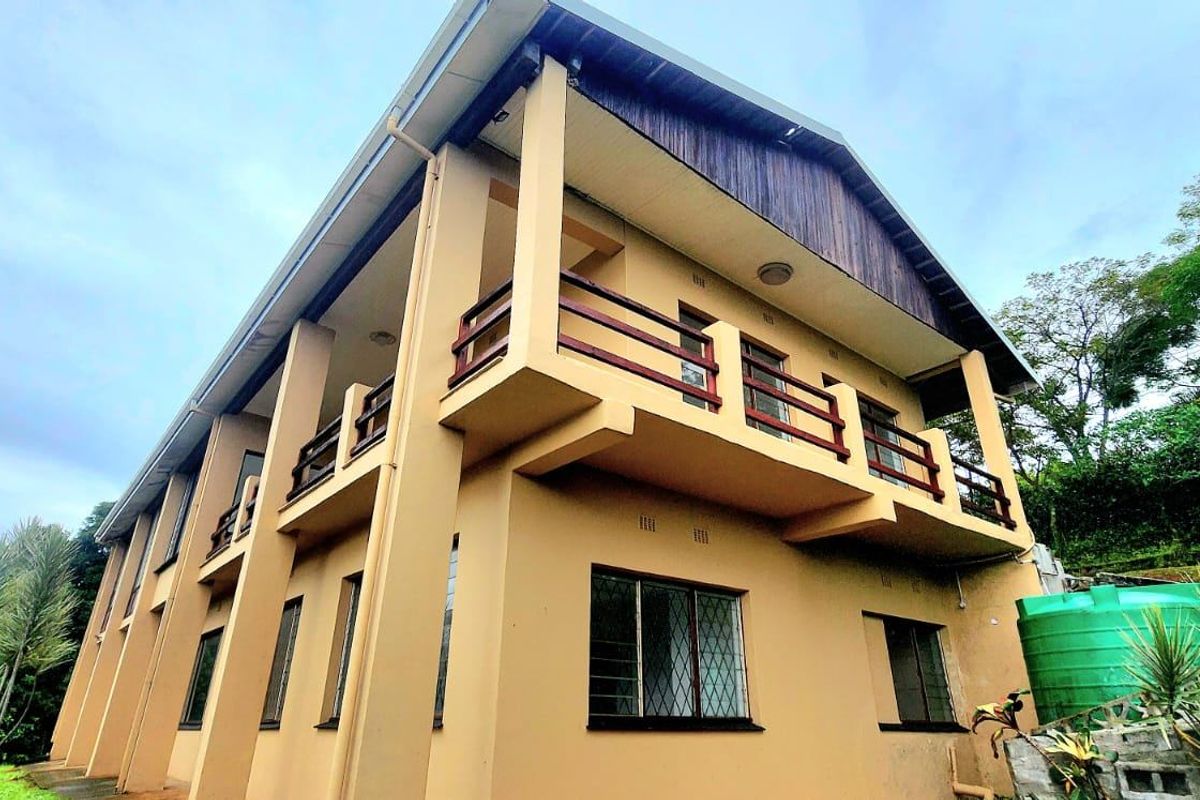 Rear view of a multi-story residential building featuring balconies, timber cladding, and a water tank set against a natural landscape.