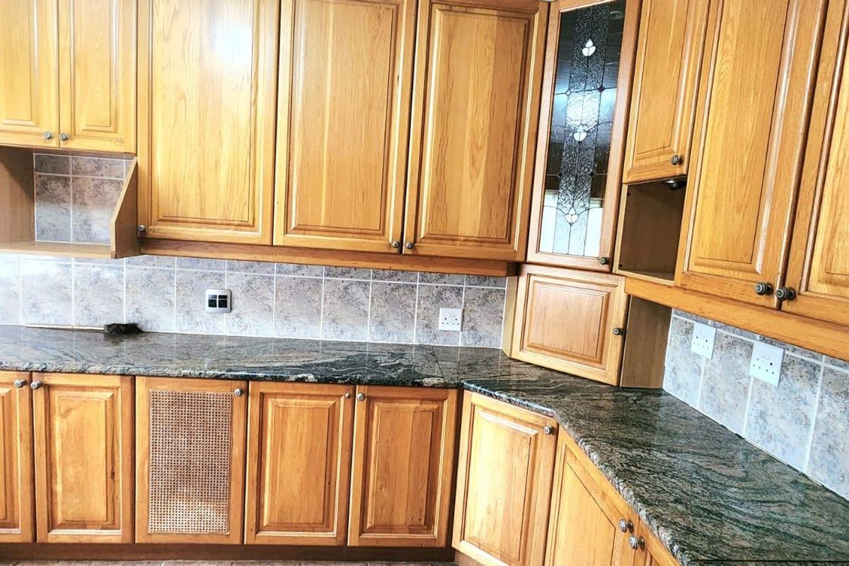 A functional kitchen featuring timber cabinetry, granite countertops, and a tiled backsplash, offering ample storage and workspace.