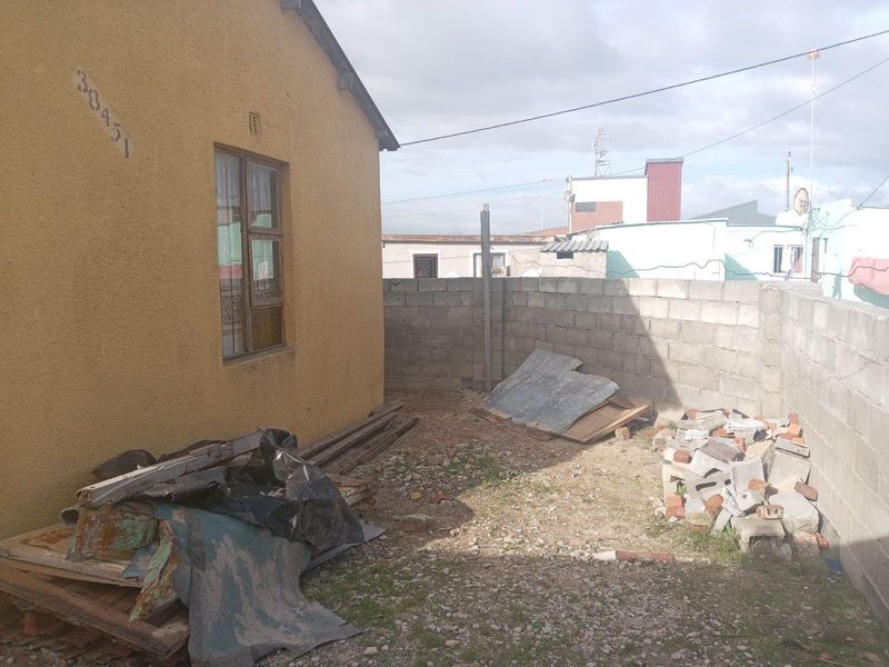 A rear exterior area featuring a stucco-finished wall and concrete block boundary fencing, currently requiring clearing and landscaping.