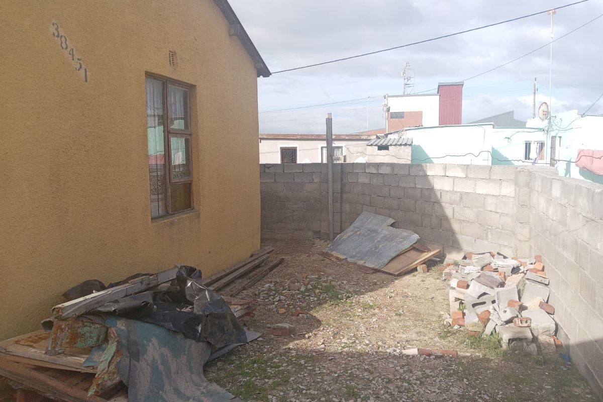 A rear exterior area featuring a stucco-finished wall and concrete block boundary fencing, currently requiring clearing and landscaping.