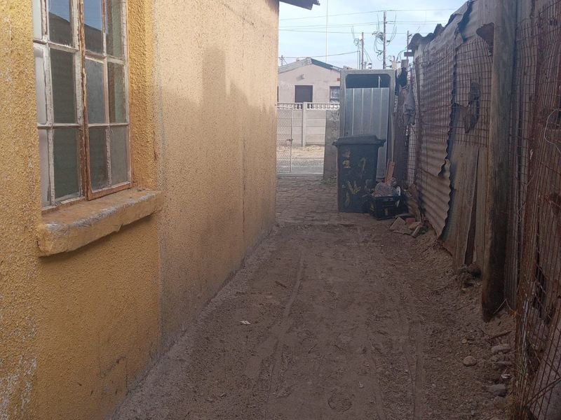 A narrow side passage of the property featuring a yellow exterior wall, steel-framed window, and corrugated metal boundary fencing.