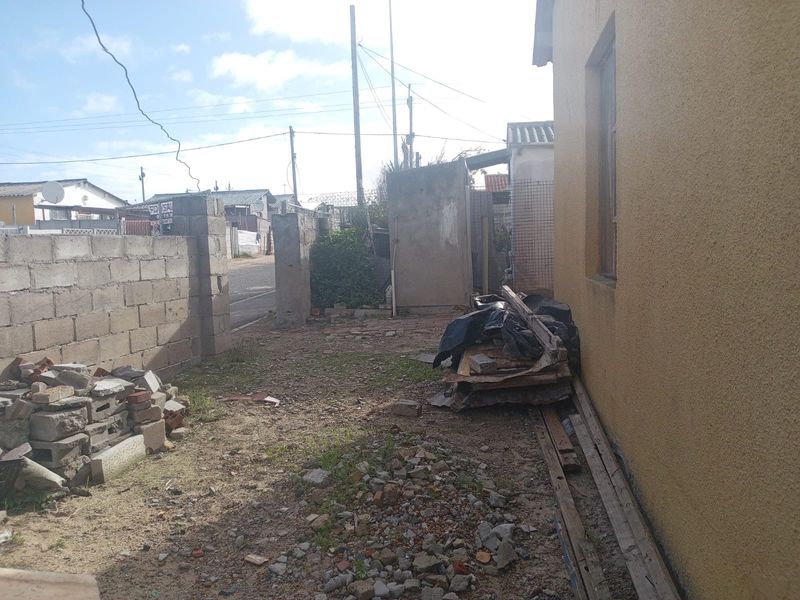 Rear exterior area featuring an unpaved yard, concrete block boundary walls, and stucco building facade, currently requiring significant landscaping and site clearance.