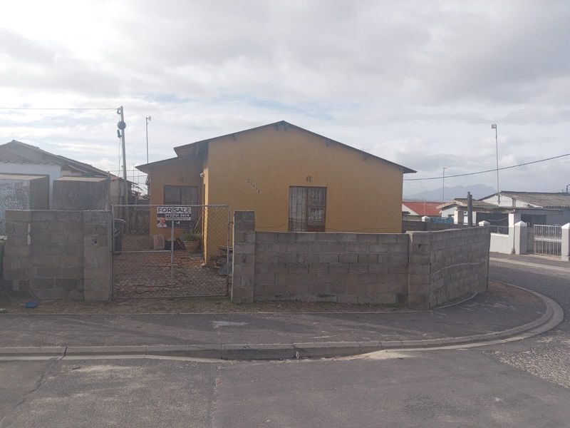 Front view of a detached house featuring a concrete block boundary wall, metal gate, and security bars on the windows.