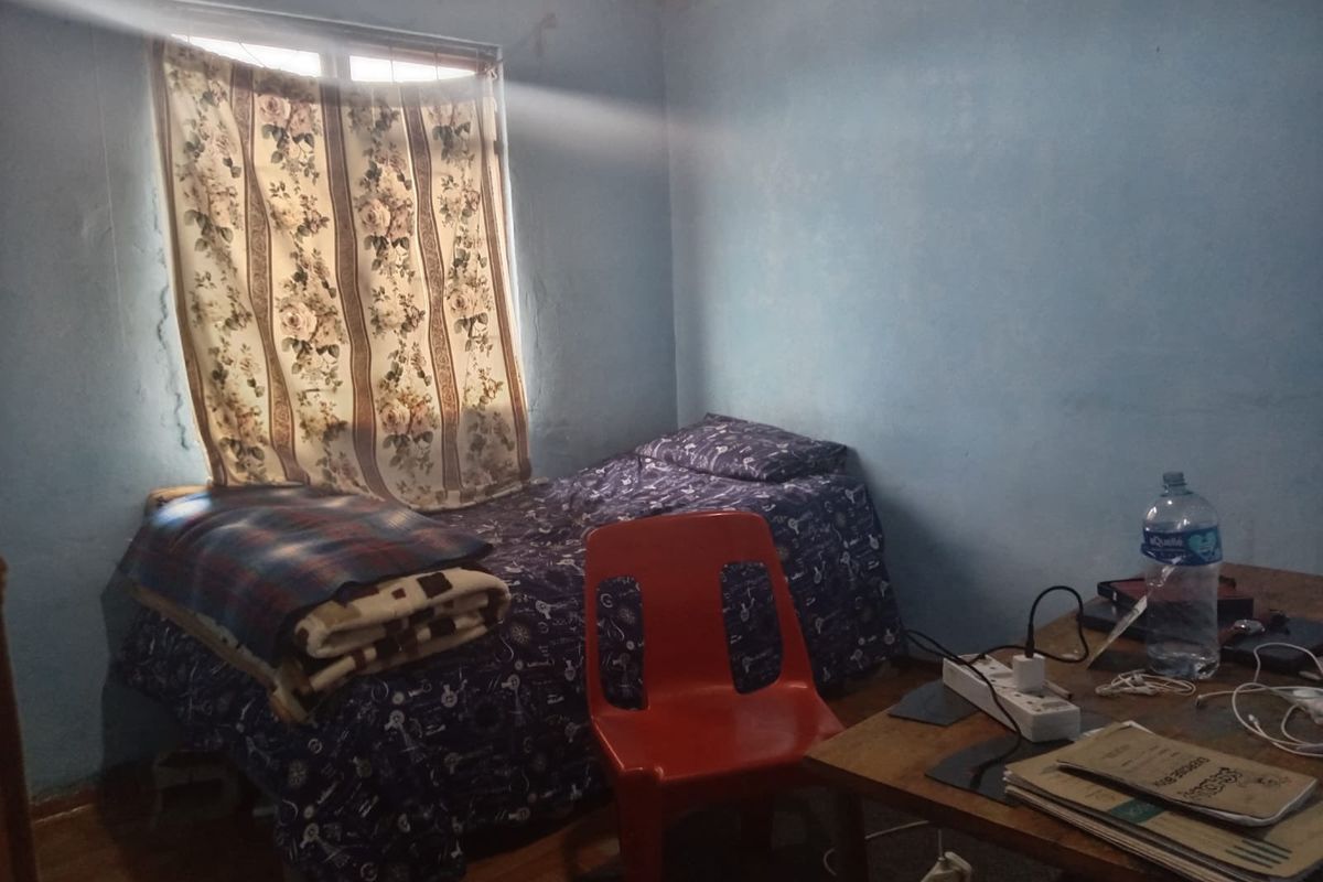 A small bedroom featuring laminate flooring and blue painted walls with visible signs of wear and plaster damage.