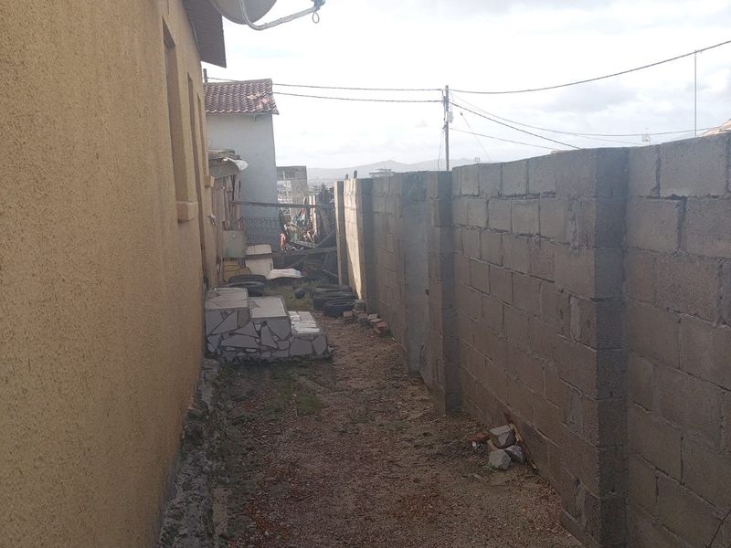 A narrow side passage featuring a concrete block boundary wall, satellite dish, and tiled steps leading to the rear of the property.