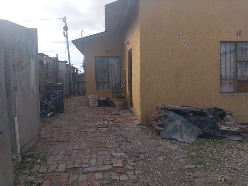 Rear exterior view of the property featuring a brick-paved pathway and yellow textured wall finish with security bars on the windows.
