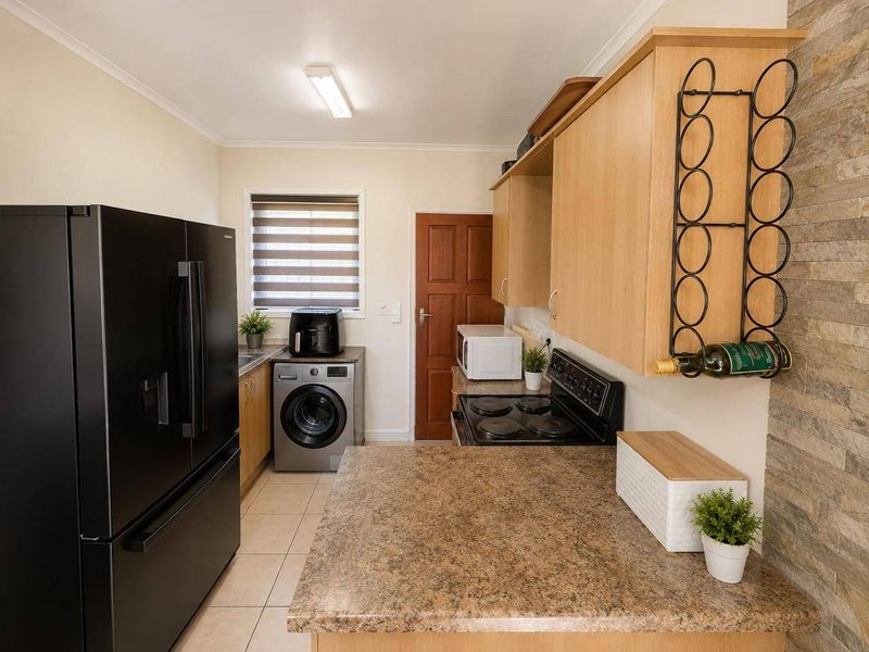 Functional kitchen featuring laminate cabinetry, stone-look countertops, an electric stove, and a decorative stone-clad feature wall with tiled flooring.