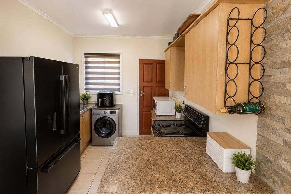 Functional kitchen featuring laminate cabinetry, stone-look countertops, an electric stove, and a decorative stone-clad feature wall with tiled flooring.