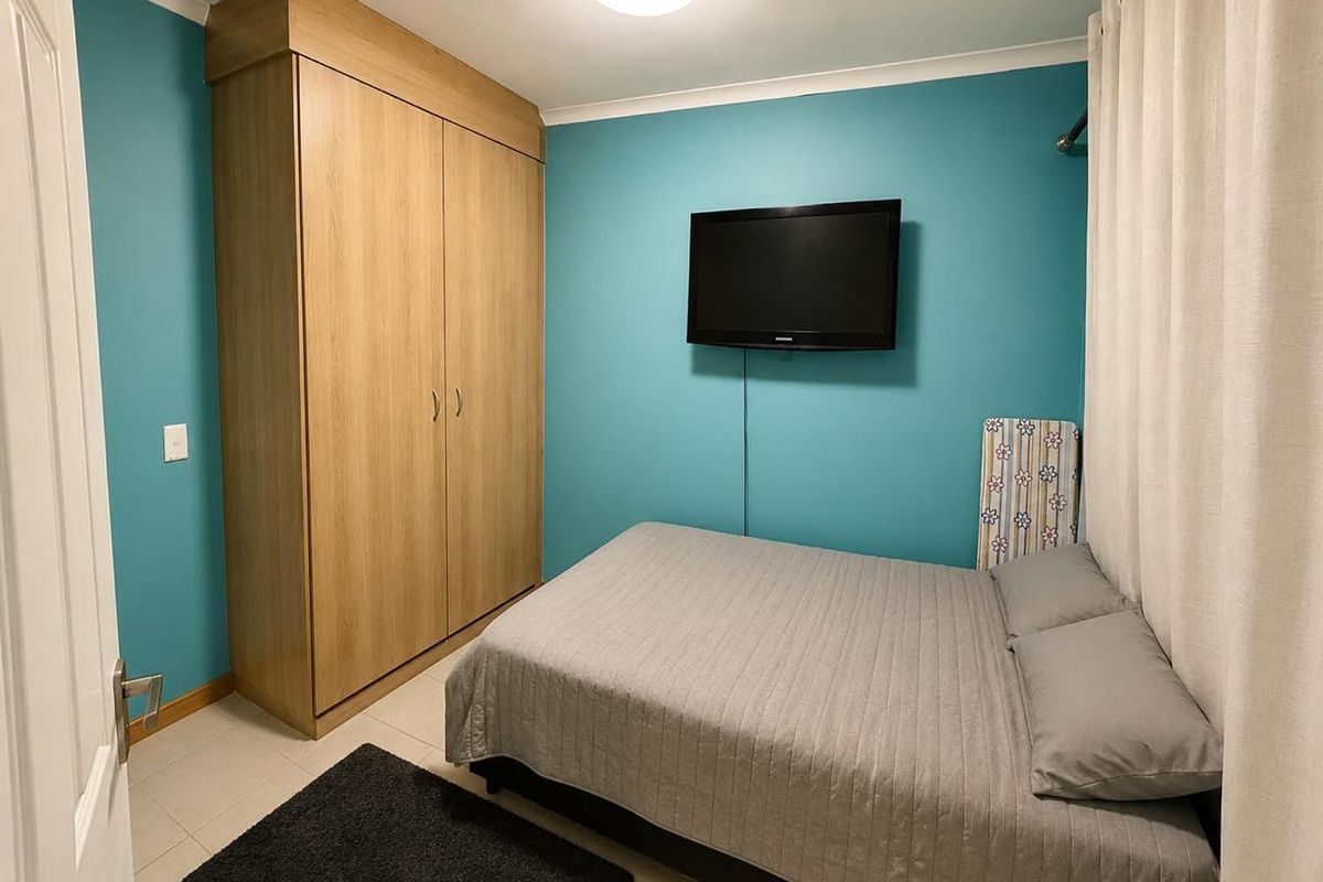 A functional bedroom featuring a built-in wooden wardrobe, tiled flooring, and teal-painted walls.
