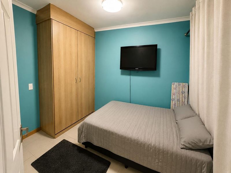 A functional bedroom featuring a built-in wooden wardrobe, tiled flooring, and teal-painted walls.