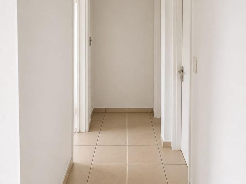 A clean, neutral hallway featuring tiled flooring and multiple internal access points, providing a bright and well-maintained transition space within the townhouse.