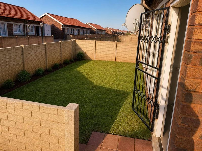 A private rear garden featuring a well-maintained lawn, paved patio area, and secure boundary walling, accessible via a security gate.