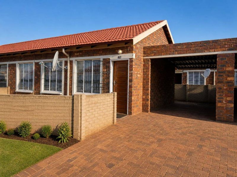Front exterior view of a face brick townhouse featuring a paved driveway, integrated carport, and well-maintained garden area.
