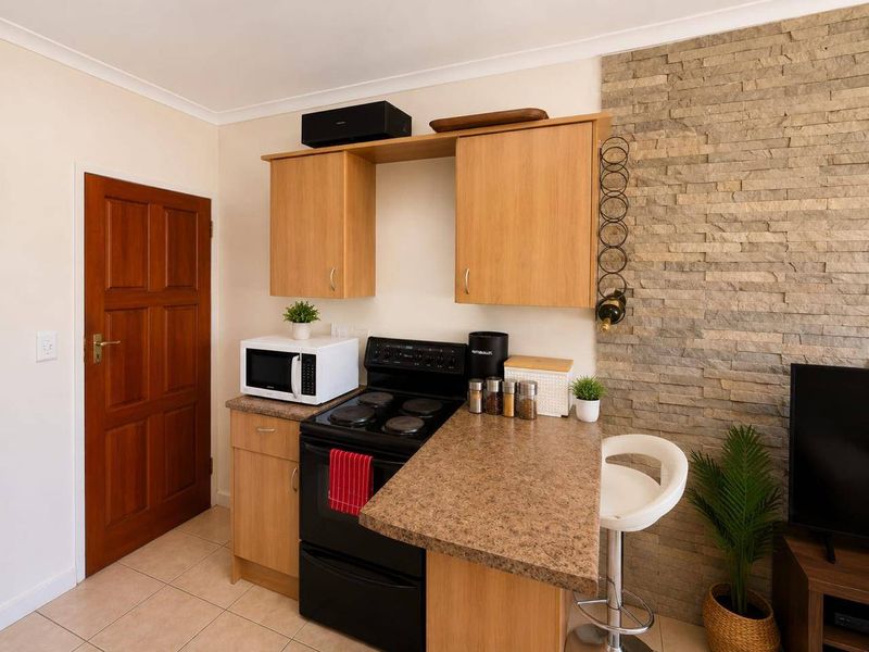Compact kitchen area featuring light wood cabinetry, a stone-look countertop, an electric stove, and a decorative stacked stone feature wall.