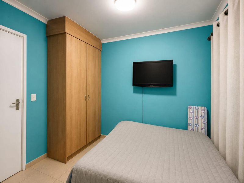 A bedroom featuring bright blue walls, tiled flooring, and a built-in wooden wardrobe.