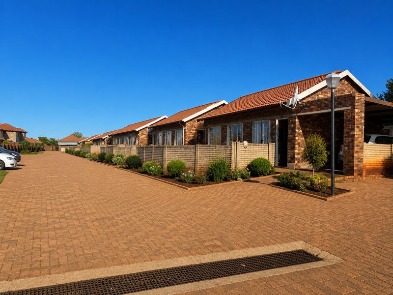 A well-maintained townhouse complex featuring face brick facades, tiled roofs, and a spacious paved driveway with integrated carport parking.