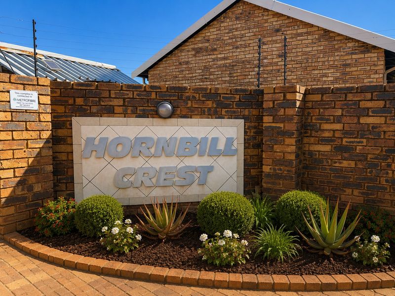 Entrance signage and landscaped garden area for Hornbill Crest townhouse complex, featuring face brick boundary walls and paved driveway access.