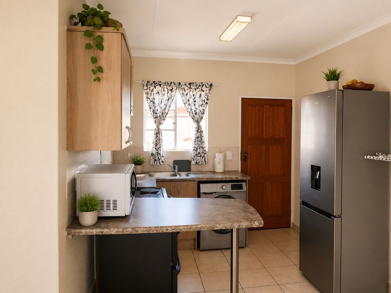 A functional kitchen featuring laminate cabinetry, tiled flooring, a stainless steel sink, and direct access to an exterior door.