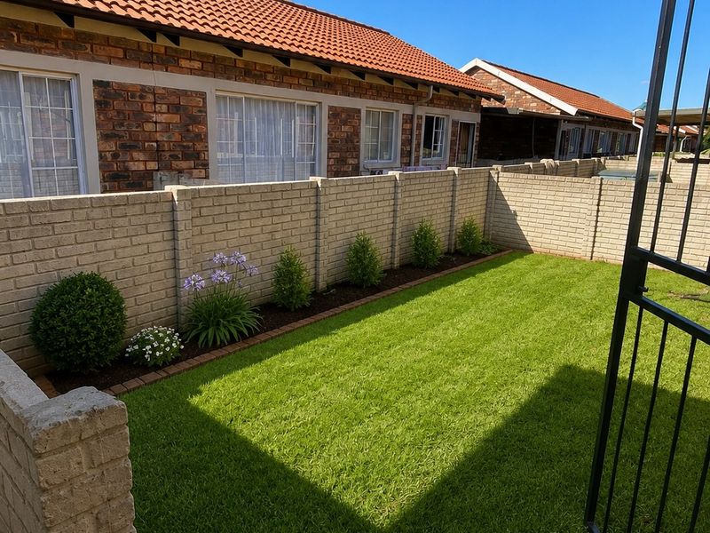 A well-maintained rear garden featuring a manicured lawn, face brick exterior walls, terracotta roof tiles, and a secure metal gate entrance.