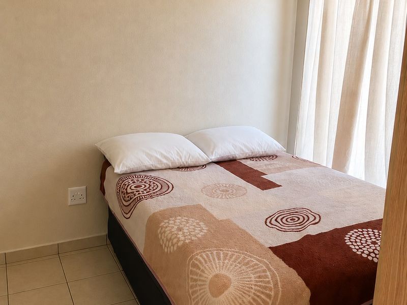 A simple bedroom featuring neutral wall tones, tiled flooring, and natural light provided by a window with curtains.