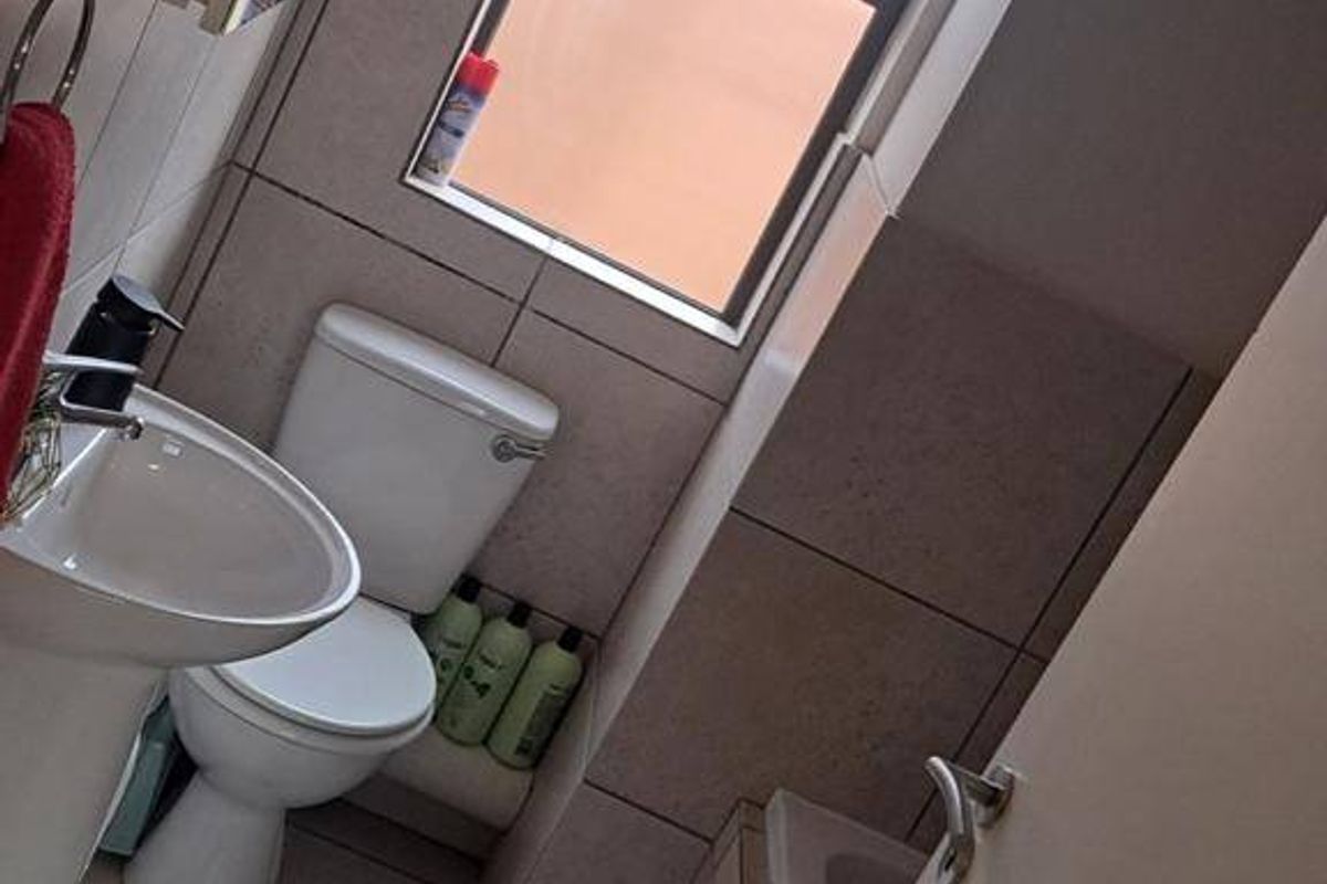 A compact bathroom featuring a pedestal basin, toilet, and bathtub with neutral wall and floor tiling.