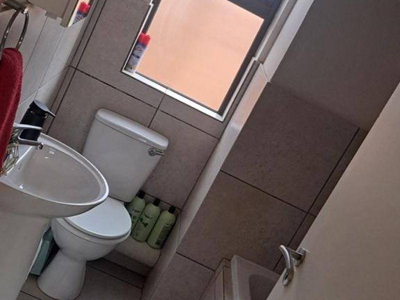 A compact bathroom featuring a pedestal basin, toilet, and bathtub with neutral wall and floor tiling.