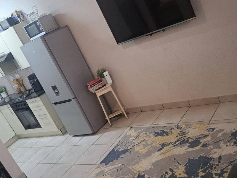 Open-plan living area featuring a compact kitchen with built-in cabinetry, oven, and hob, seamlessly flowing into the lounge space with tiled flooring.