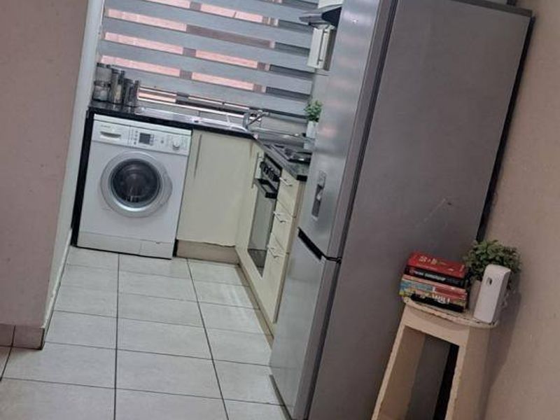 A compact kitchen featuring tiled flooring, built-in cabinetry, an integrated oven, and a hob, providing a functional workspace within the townhouse.