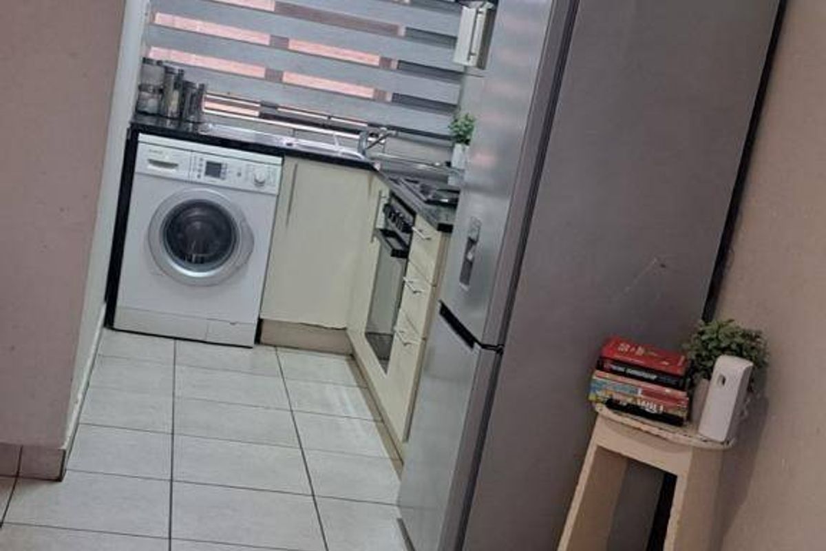 A compact kitchen featuring tiled flooring, built-in cabinetry, an integrated oven, and a hob, providing a functional workspace within the townhouse.