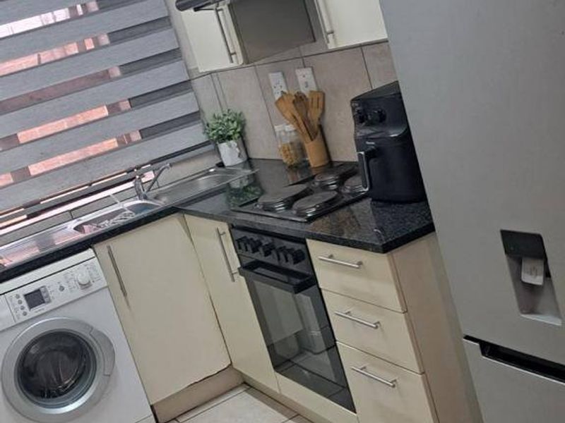 Compact kitchen featuring built-in cabinetry, granite countertops, integrated oven and hob, and tiled flooring with a dedicated space for a washing machine.