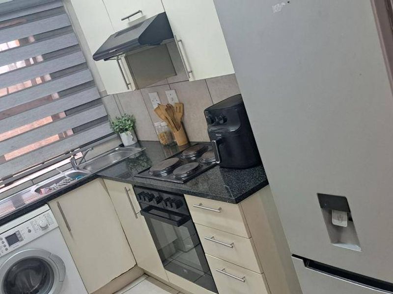 Compact kitchen featuring built-in cabinetry, granite countertops, integrated electric hob and oven, extractor fan, and tiled flooring.