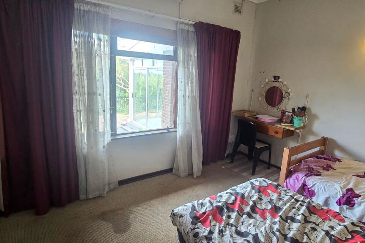 A bedroom featuring a built-in cupboard, wall-mounted lighting, and a large window, currently requiring cosmetic updates to the flooring and wall finishes.
