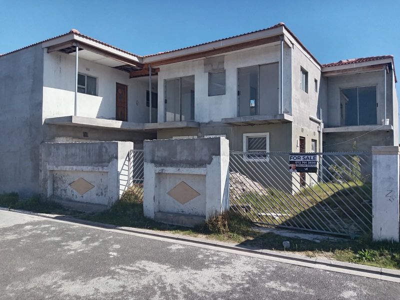 Exterior view of a multi-level apartment building under construction, featuring unfinished plaster, metal security fencing, and balcony access.