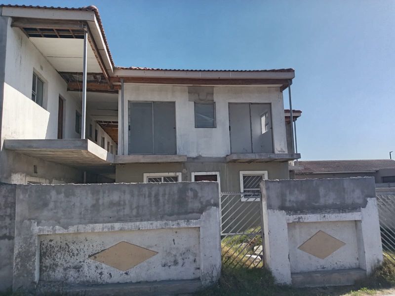 Front exterior view of a multi-story apartment building showing unfinished plaster, exposed roof eaves, and a concrete boundary wall with metal gate.
